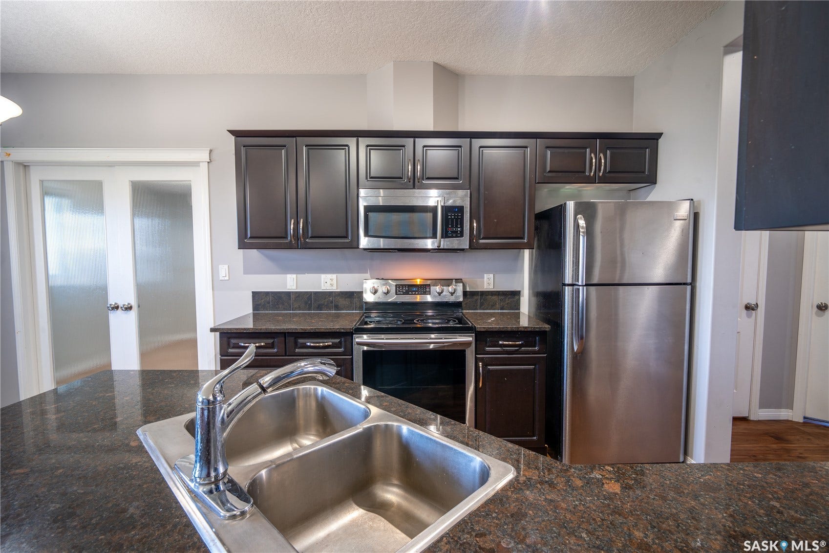 Kitchen featuring dark wood-finish cabinetry, stainless steel appliances, and a double basin sink