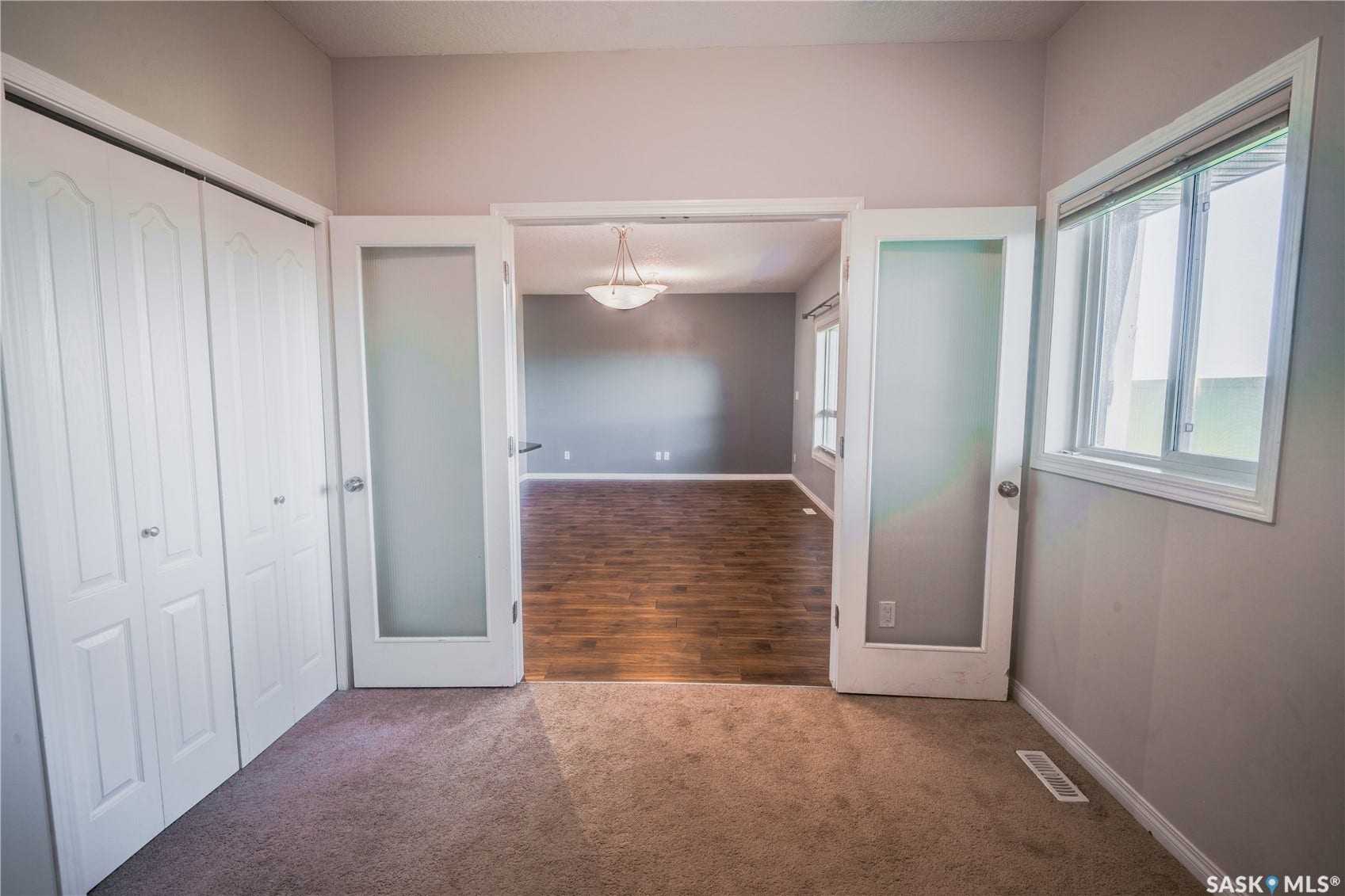 Carpeted flooring, white bi-fold closet doors, a white framed window, and frosted glass French doors