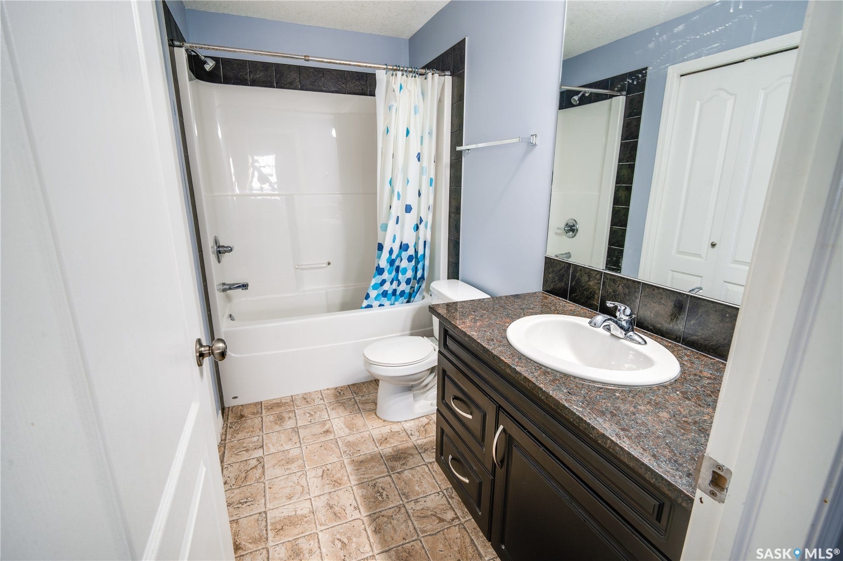 Spacious bathroom with a white tub-shower combination, dark vanity, integrated sink, and tiled flooring