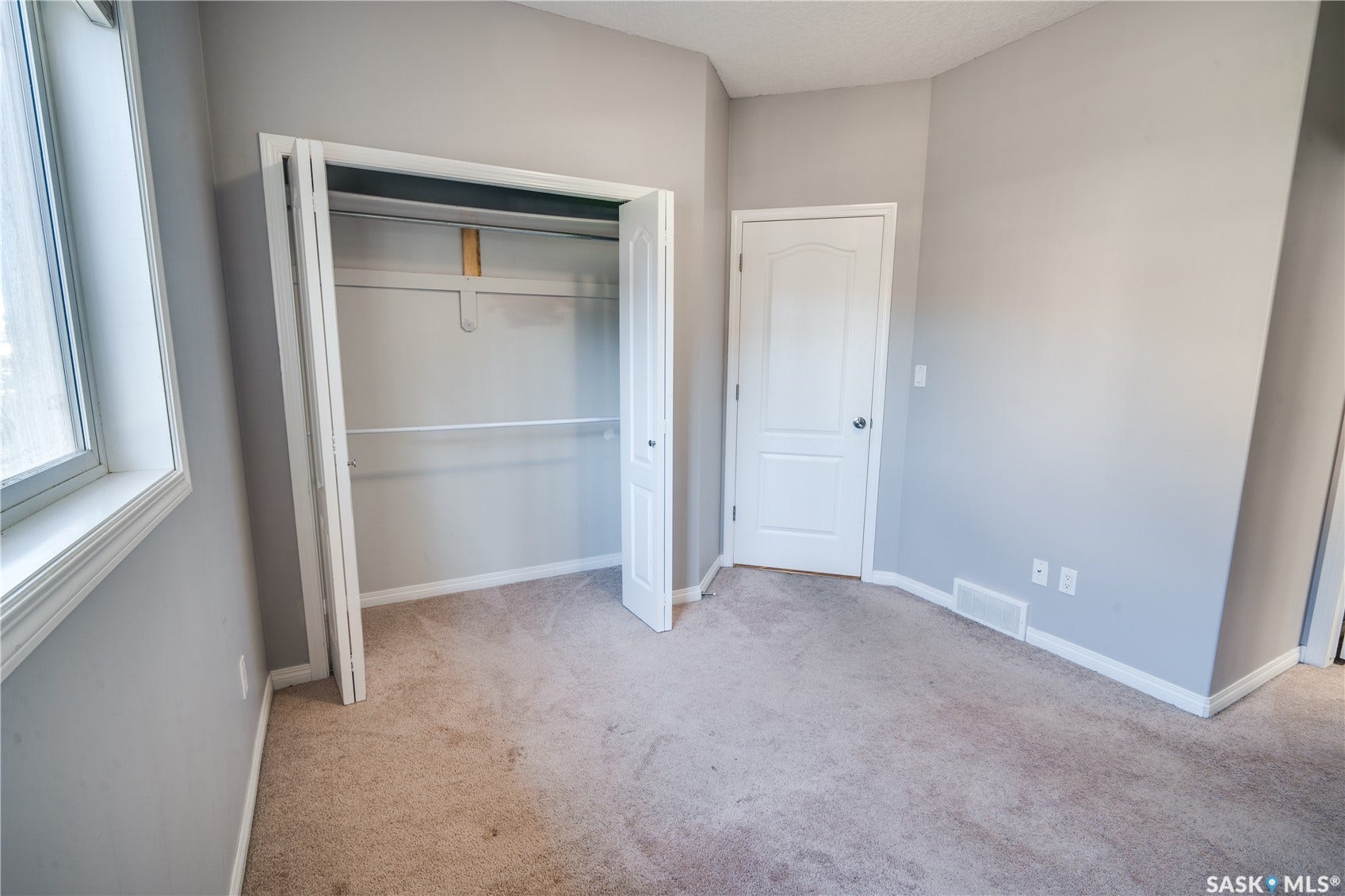 Neutral-toned carpeting, ample natural light from a large window, a bi-fold door closet with shelving and hanging rods, and a paneled interior door