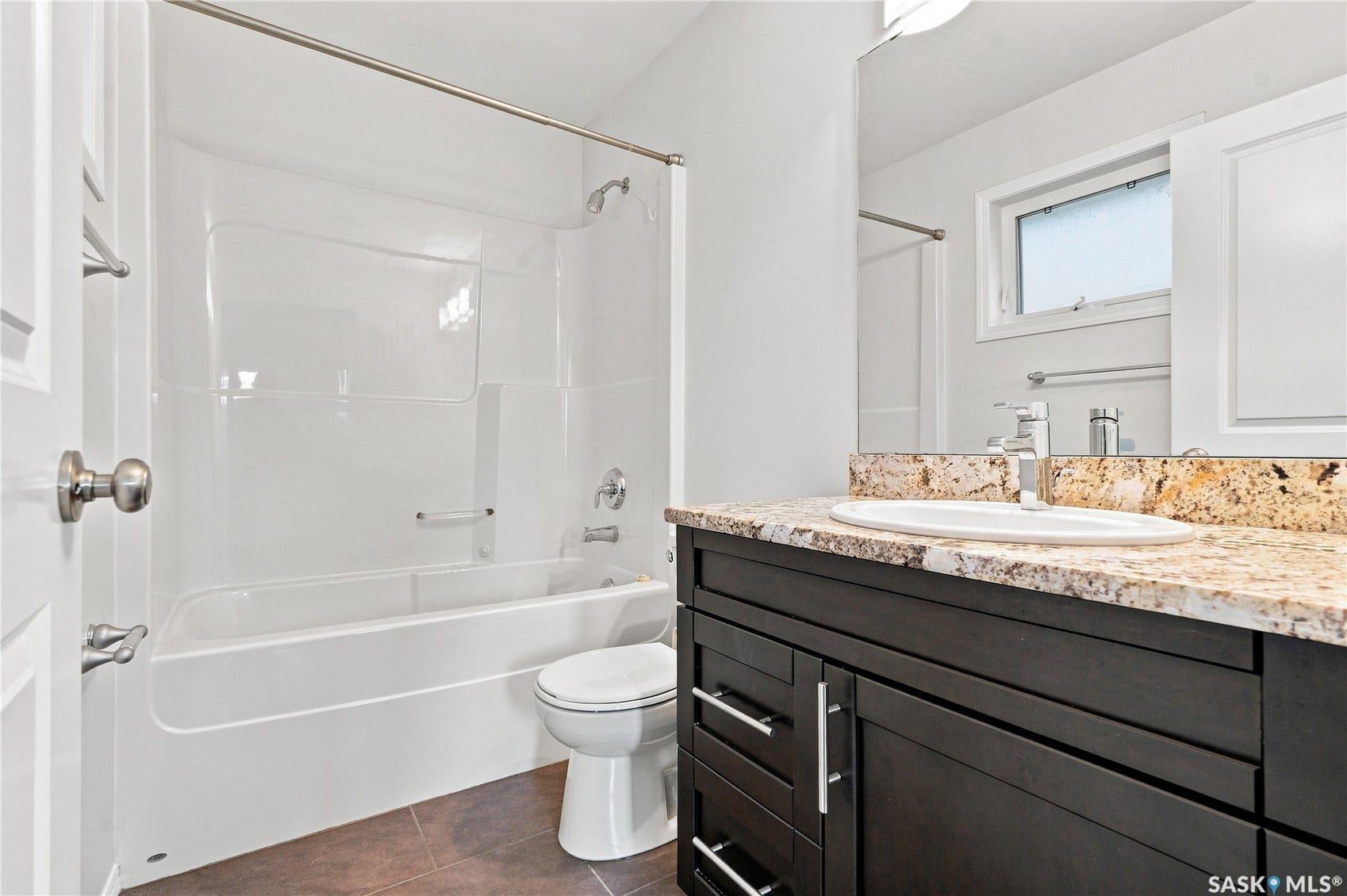 White one-piece bathtub and shower combination, dark wood-finish vanity with chrome hardware, oval undermount sink, stone-finish countertop, and a window with white trim