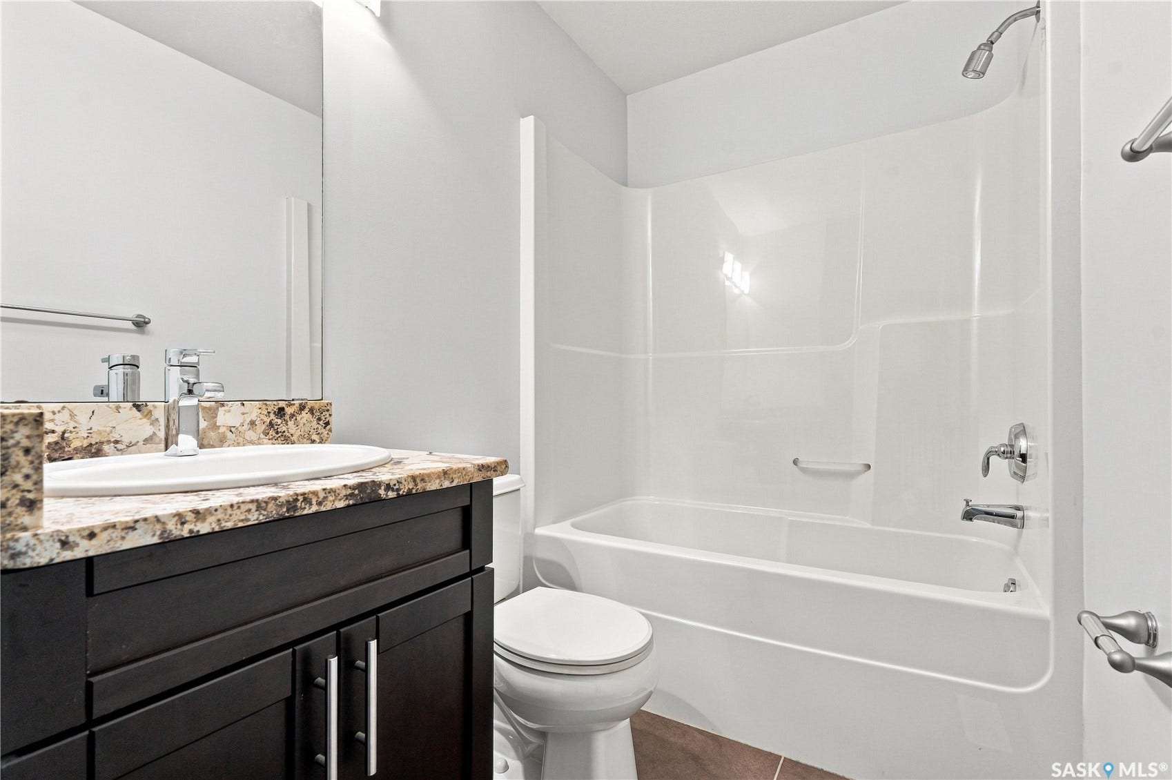 Bathroom featuring a dark wood-finish vanity with a granite-style countertop, an undermount sink, and a combination shower/bathtub with a white surround
