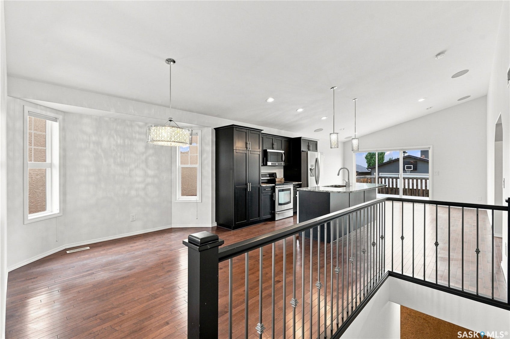 Open-concept main floor featuring wood-finish flooring, a contemporary kitchen with dark cabinetry and stainless steel appliances, a center island with pendant lighting, and a bay window area