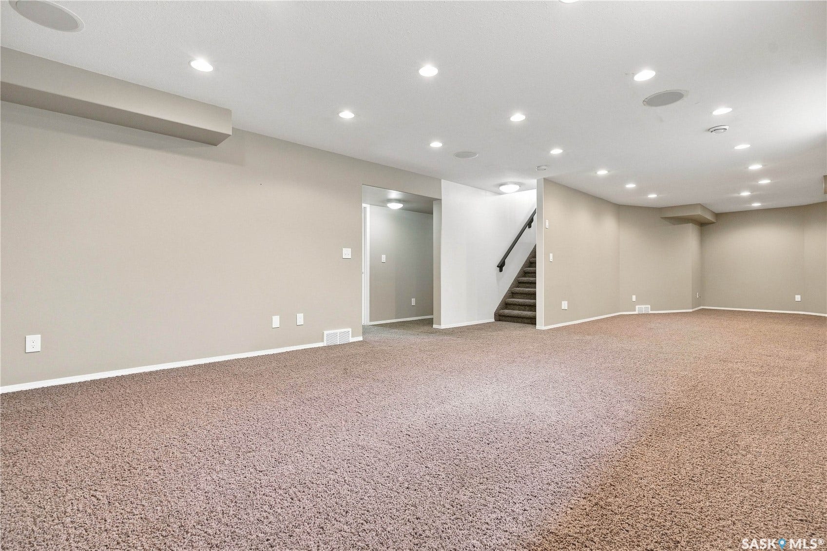 Expansive carpeted area featuring recessed lighting, a staircase with dark wood-finish handrails, and neutral wall tones