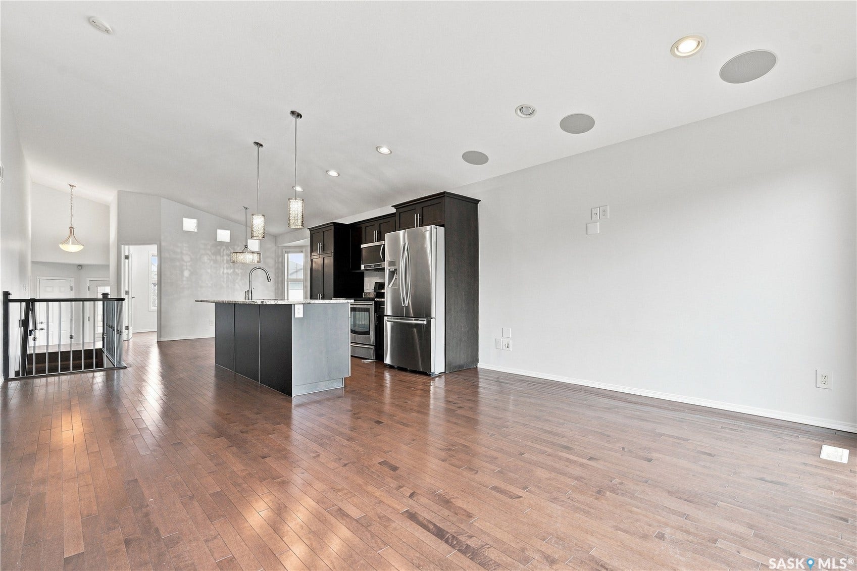 Hardwood flooring throughout, kitchen island with sink, stainless steel appliances, dark wood-finish cabinetry, and recessed lighting