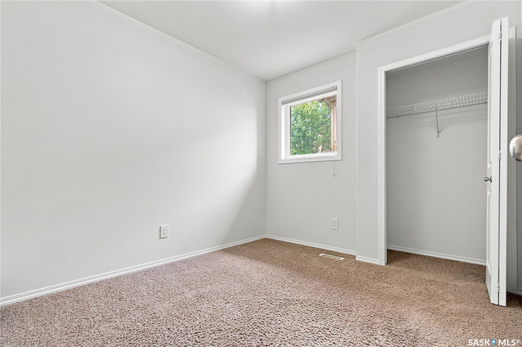 Neutral tone wall paint, carpet flooring, single window, and a closet with wire shelving