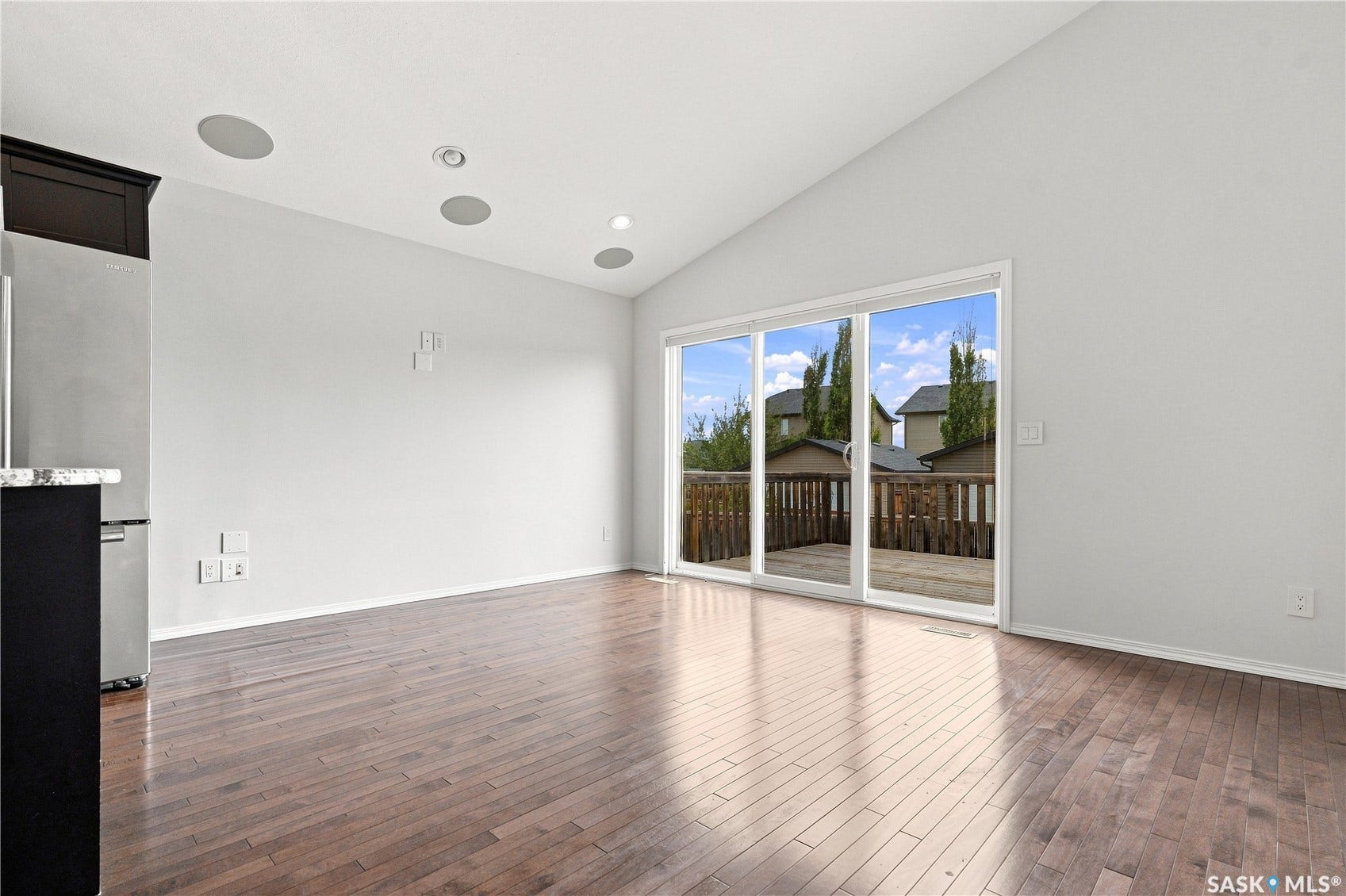 Vaulted ceiling with recessed lighting and integrated speakers, wood-finish flooring, and sliding glass doors leading to a wooden deck