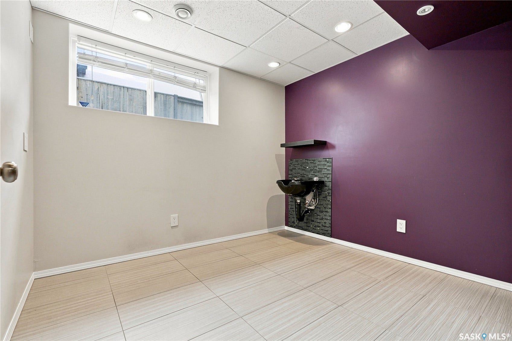 Recessed lighting, drop ceiling, wall-mounted sink with tile backsplash, and light-toned tile flooring
