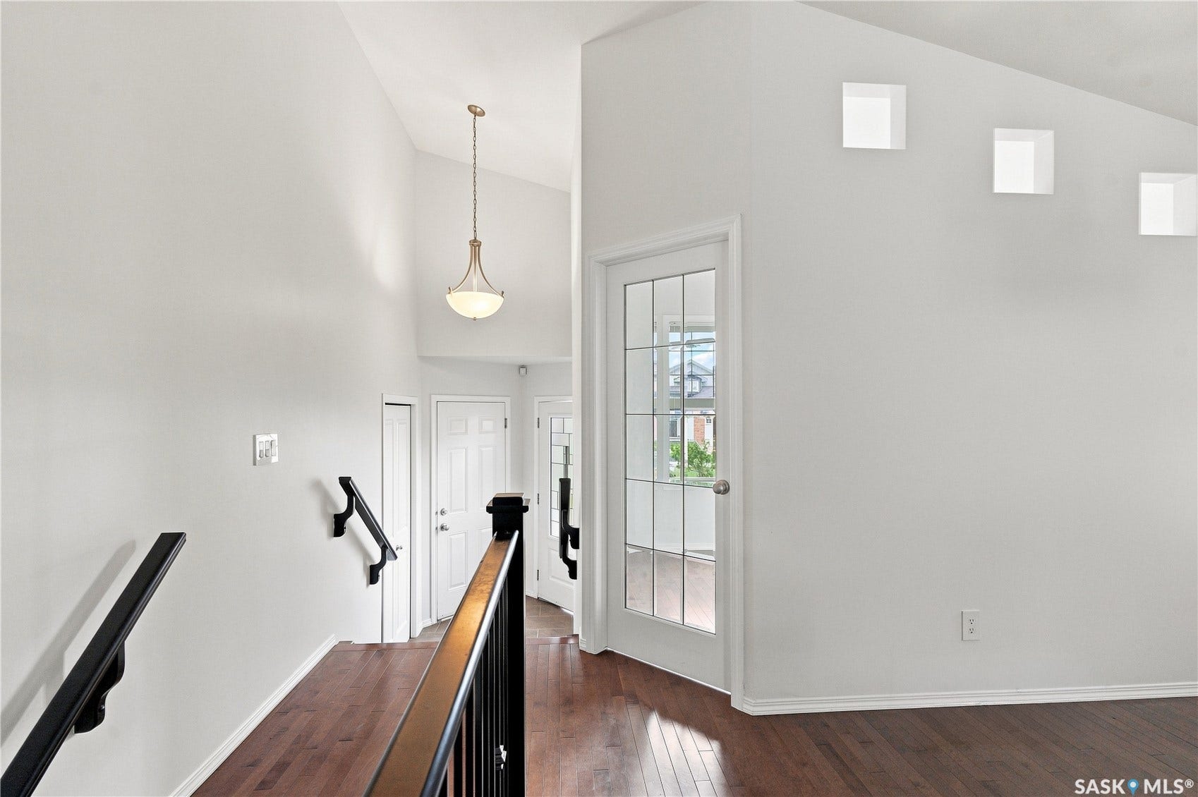 Vaulted ceilings with a suspended light fixture, dark wood-finish flooring, and a white French door