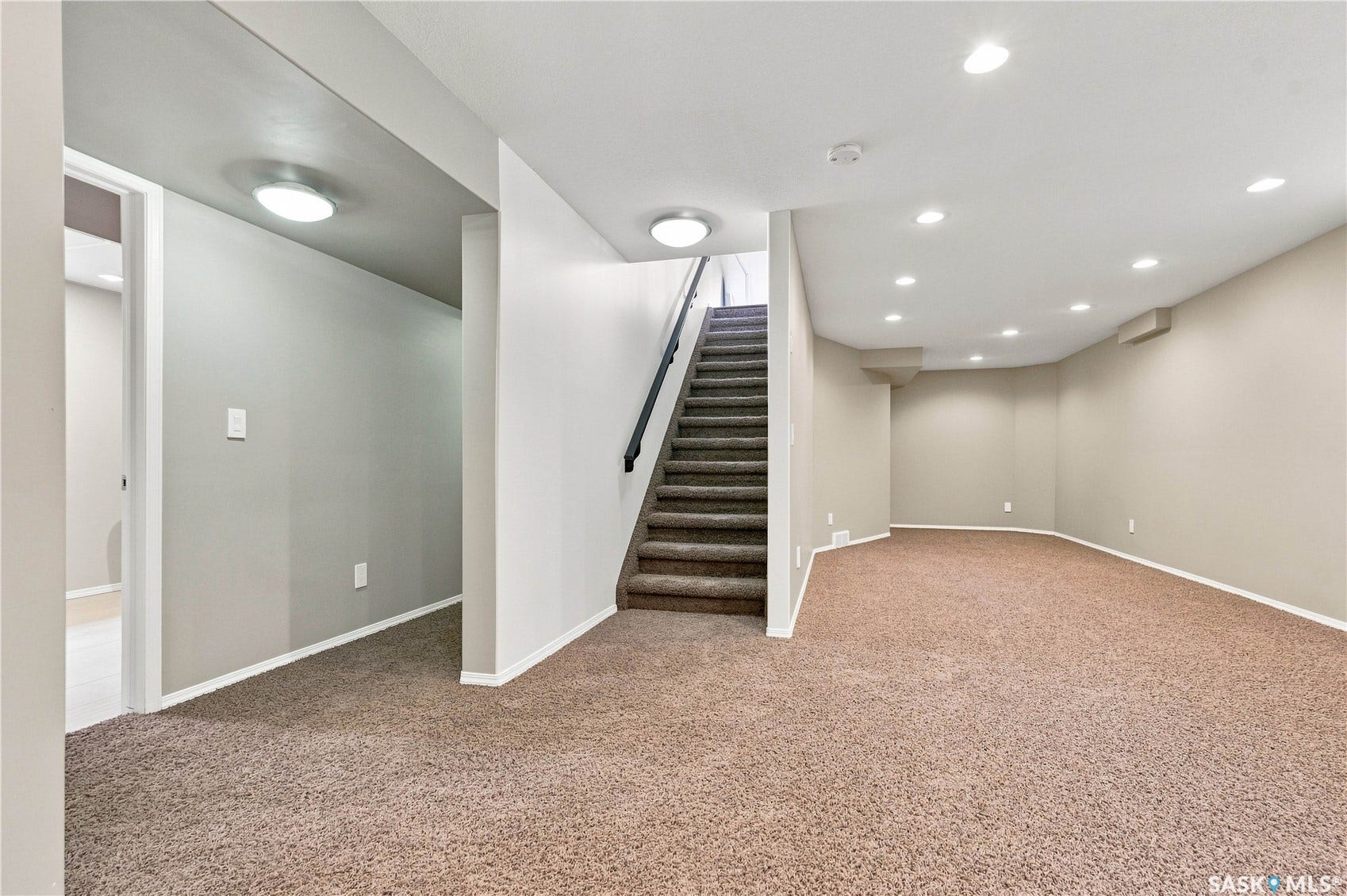 Spacious carpeted area with recessed lighting, neutral wall finishes, and a carpeted staircase