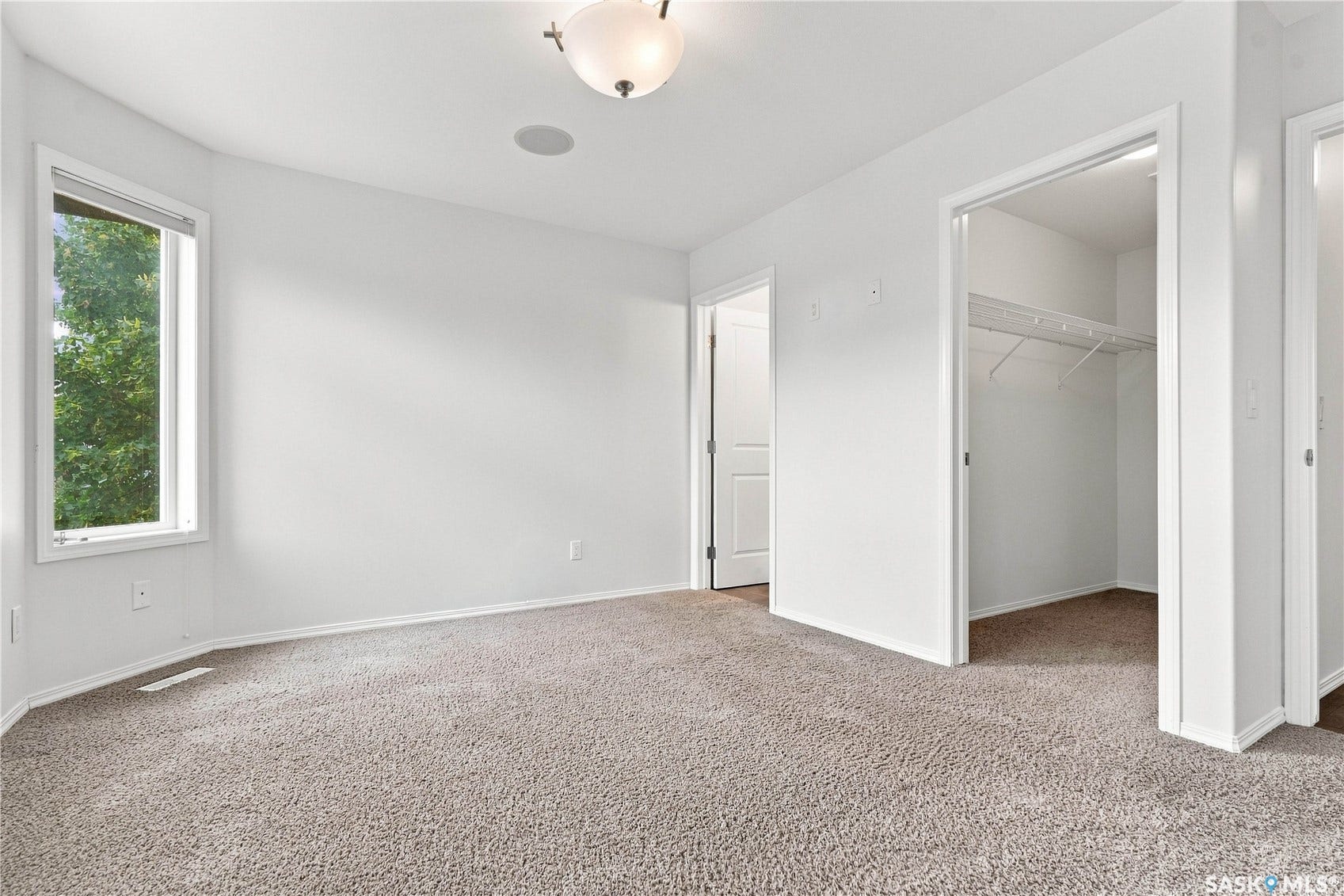 Recessed ceiling speaker, overhead flush mount light fixture, wall-to-wall carpeting, window with white trim, and a closet with shelving