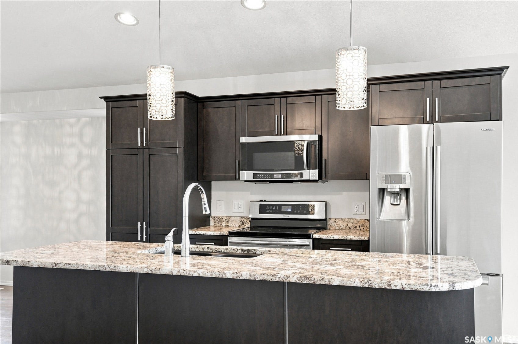 Center island with a built-in sink, dark wood-finish cabinetry, stainless steel appliances, and recessed lighting