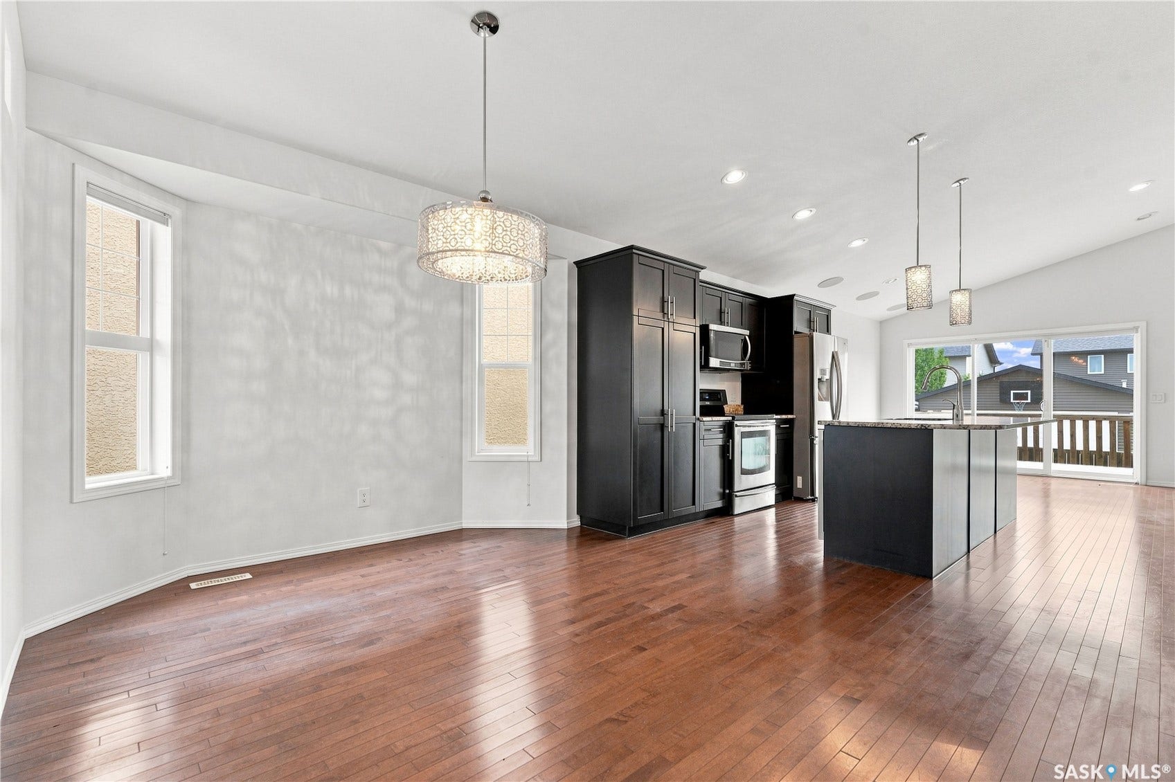 Wood-finish flooring, vaulted ceiling, black cabinetry, stainless steel appliances, and a kitchen island with pendant lighting