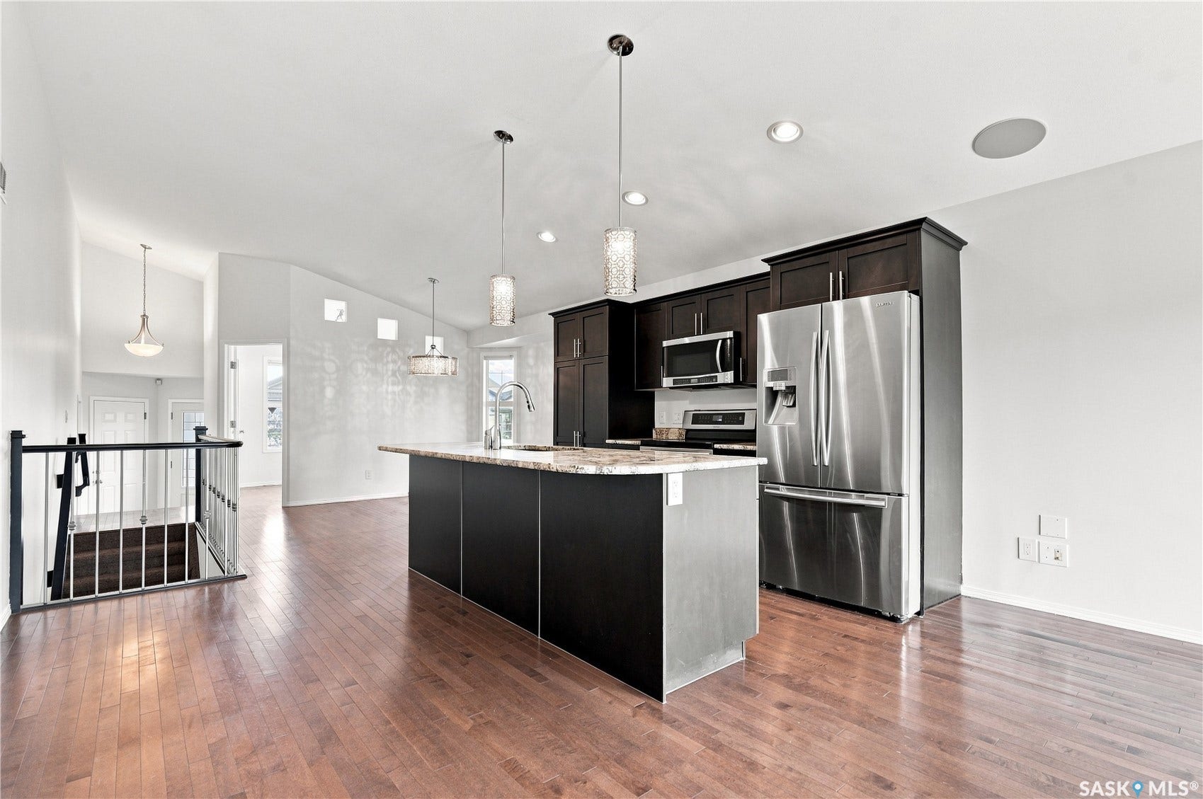 Kitchen with stainless steel appliances, dark wood-finish cabinetry, and a central island with a sink and pendant lighting
