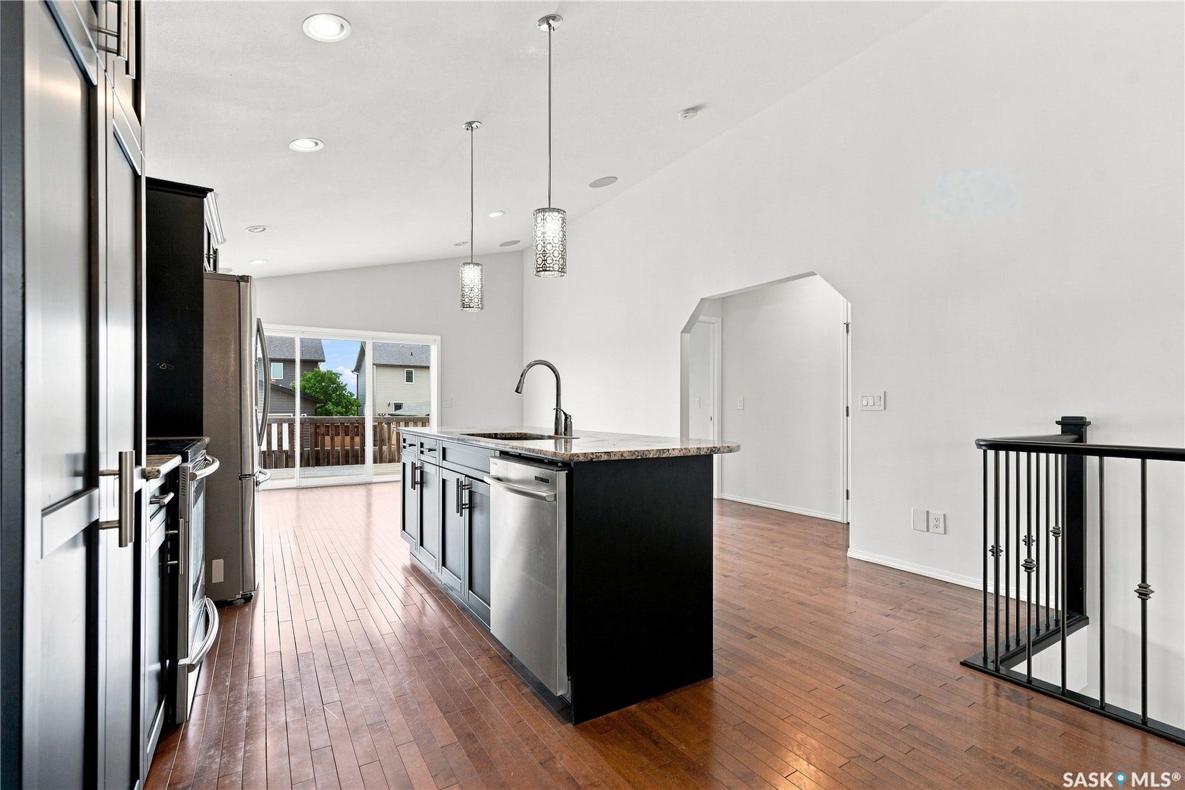 Kitchen island with integrated sink, stainless steel appliances, wood-finish flooring, recessed lighting, and a sliding glass door