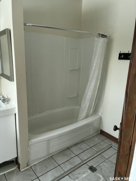 White bathtub with integrated shower, chrome shower rod, and tiled flooring
