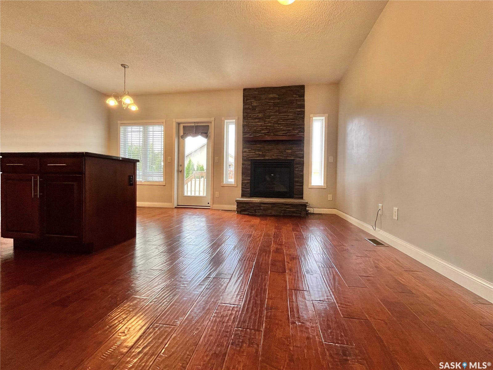 Wood-finish flooring, stone-clad fireplace, built-in island cabinetry, recessed lighting, and a white paneled door
