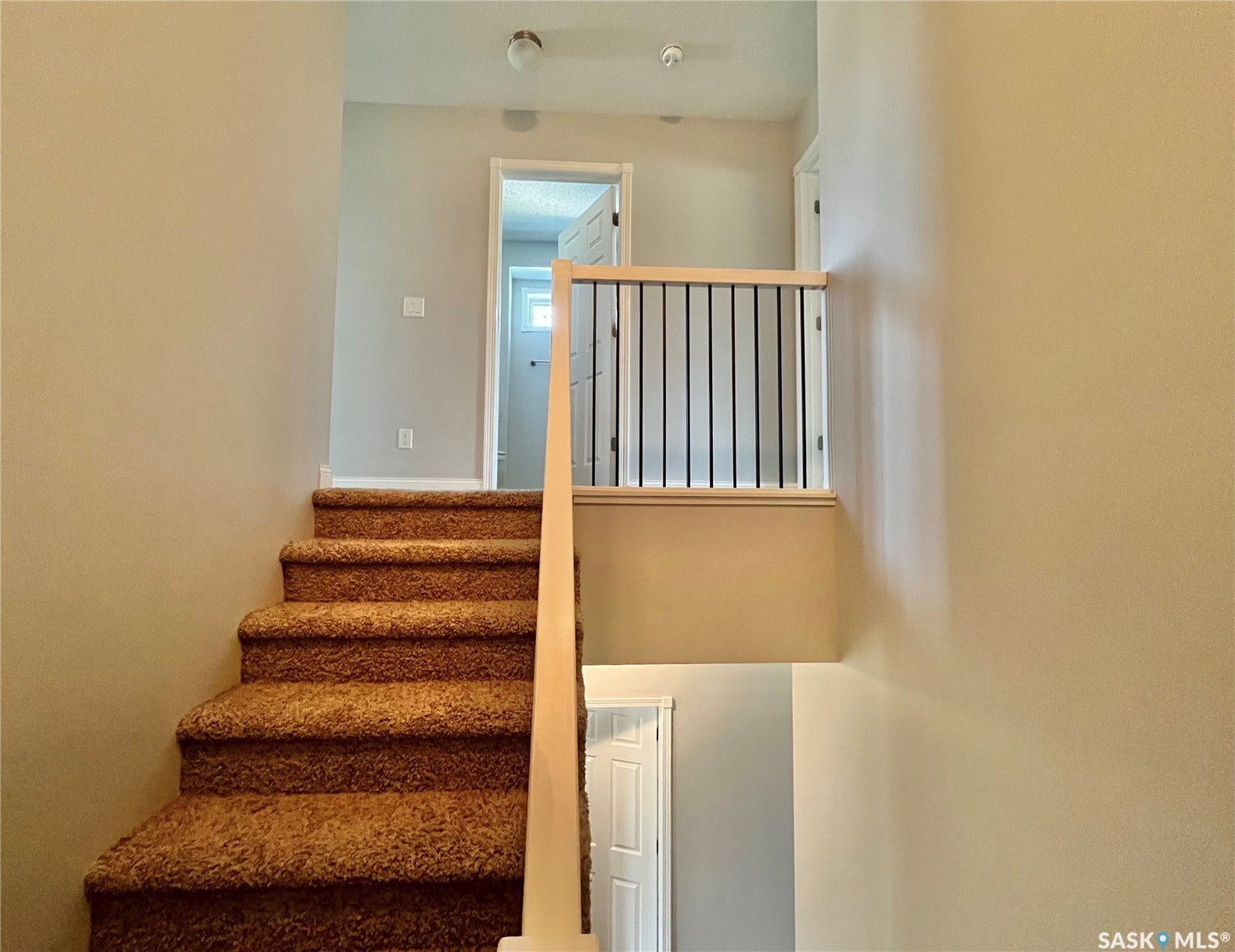Staircase with carpeted treads and risers, featuring a light wood newel post and a metal spindle railing