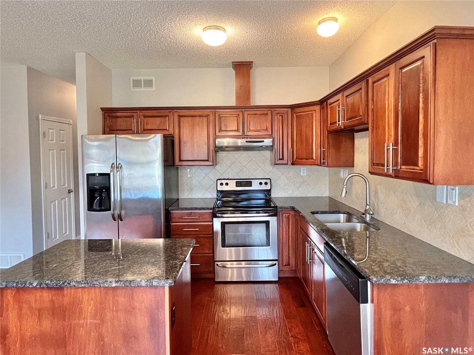 Kitchen featuring wood-finish cabinetry, dark stone-finish countertops, stainless steel appliances, a double basin sink with a gooseneck faucet, and tile backsplash