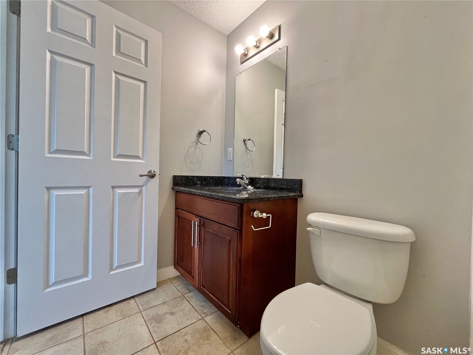 Vanity with dark wood cabinetry, a dark countertop, and a rectangular sink
