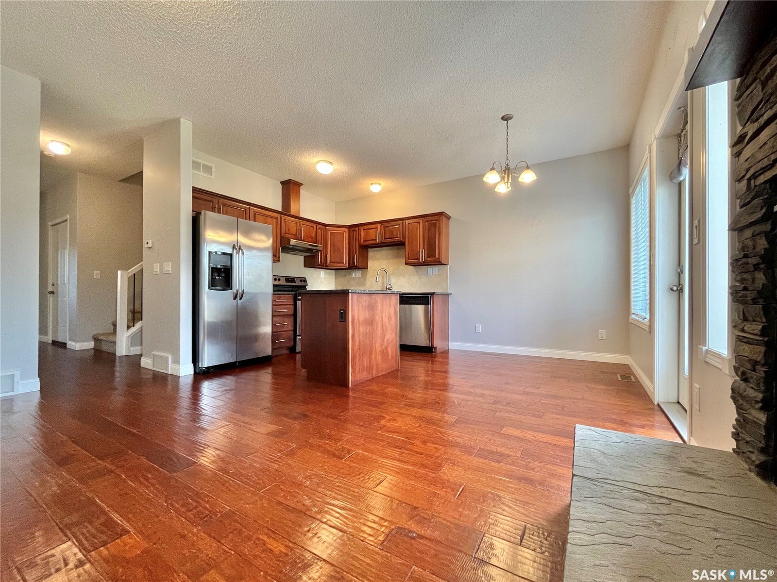 Wood-finish flooring, cherry-toned cabinetry, stainless steel appliances, kitchen island, and a stone-clad fireplace