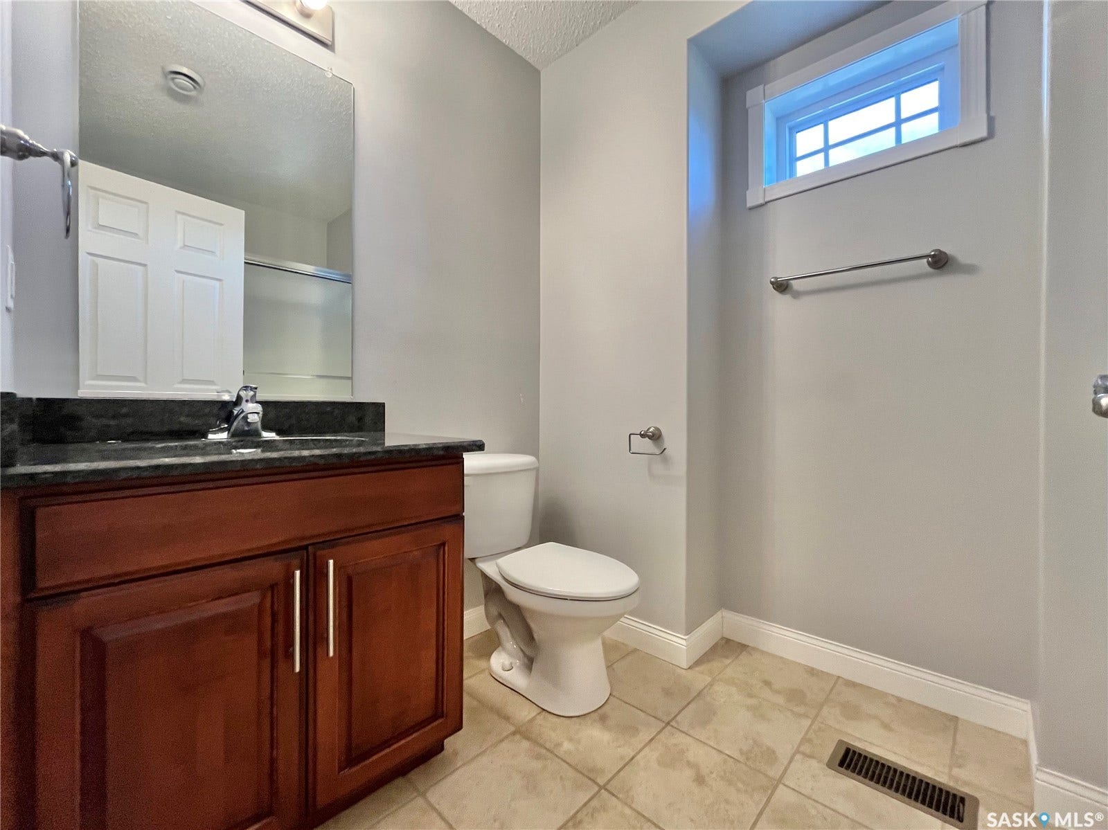 Wood-finish vanity with dark countertop, undermount sink, and polished chrome faucet