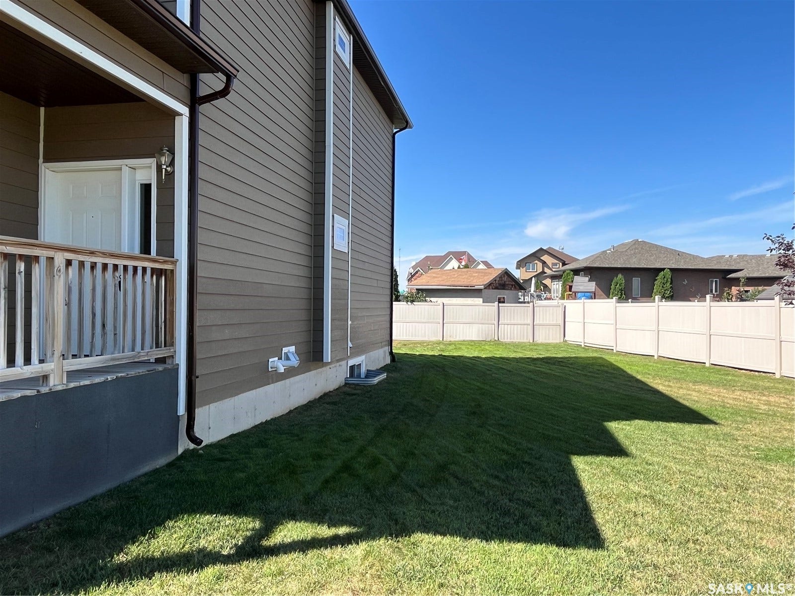 Manicured lawn with a privacy fence and a side-entry porch featuring a wooden railing