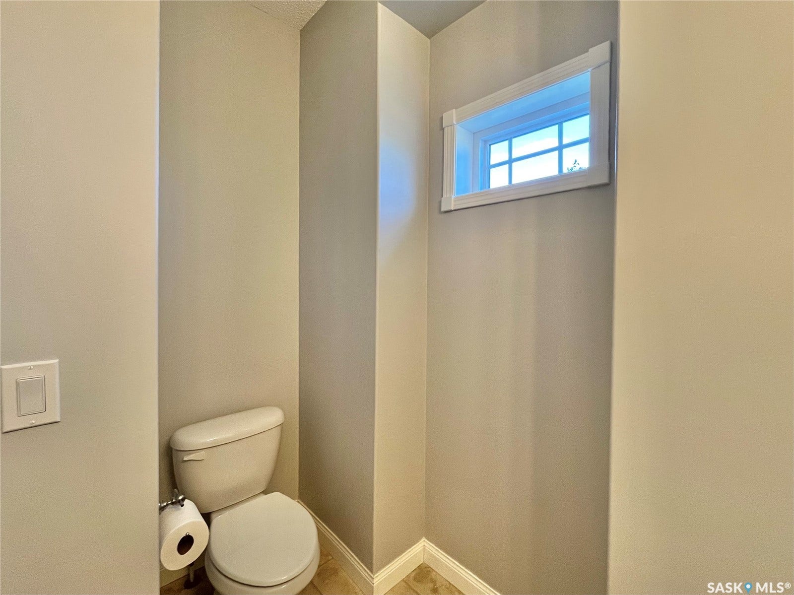 Recessed toilet alcove with a frosted transom window, light neutral wall paint, and tiled flooring