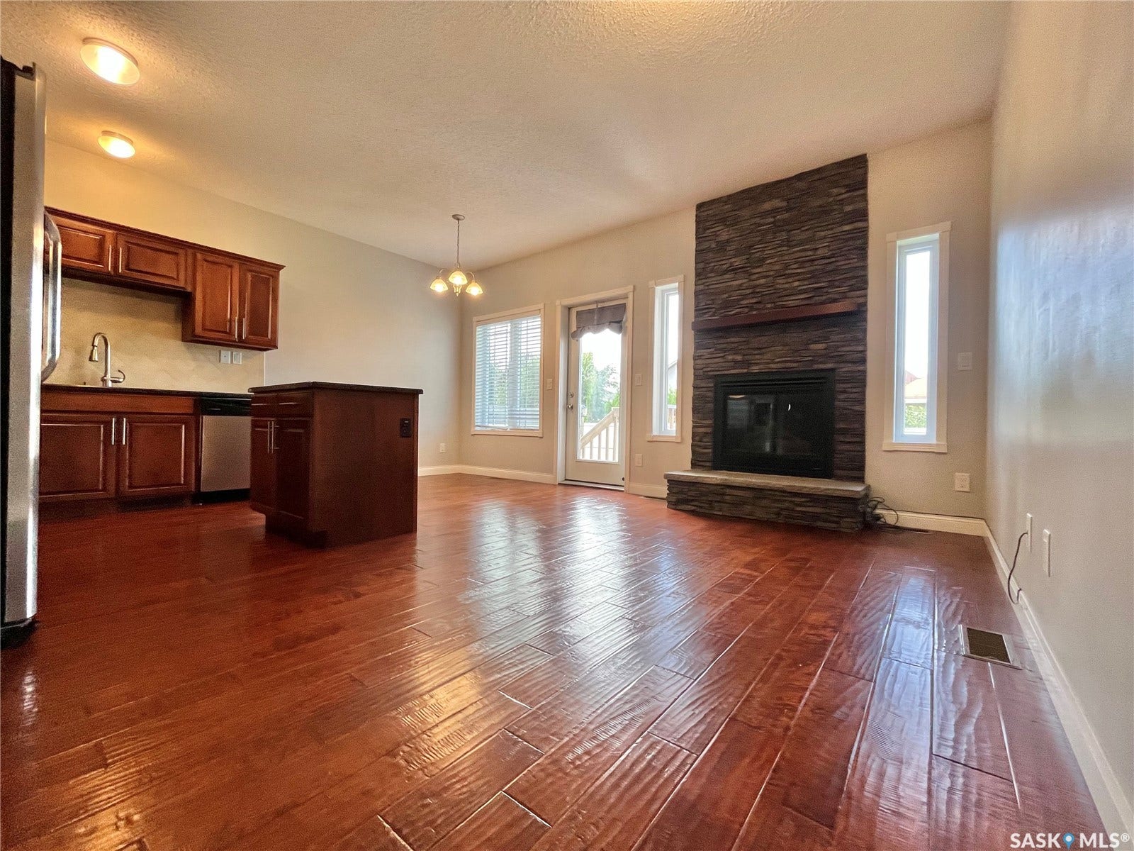 Open-concept living space with wood-finish flooring, a stone-clad fireplace, and a kitchen island with storage