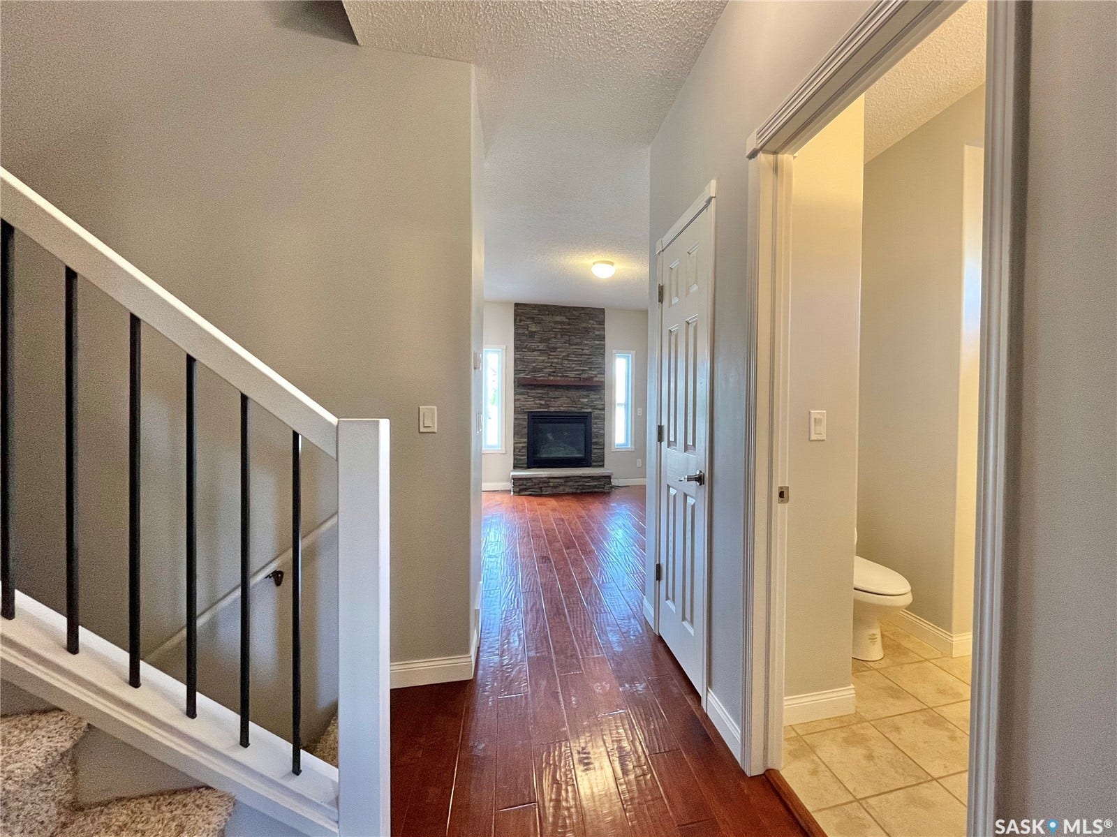 Staircase with white railing and black balusters, wood-finish flooring, and a stone-clad fireplace