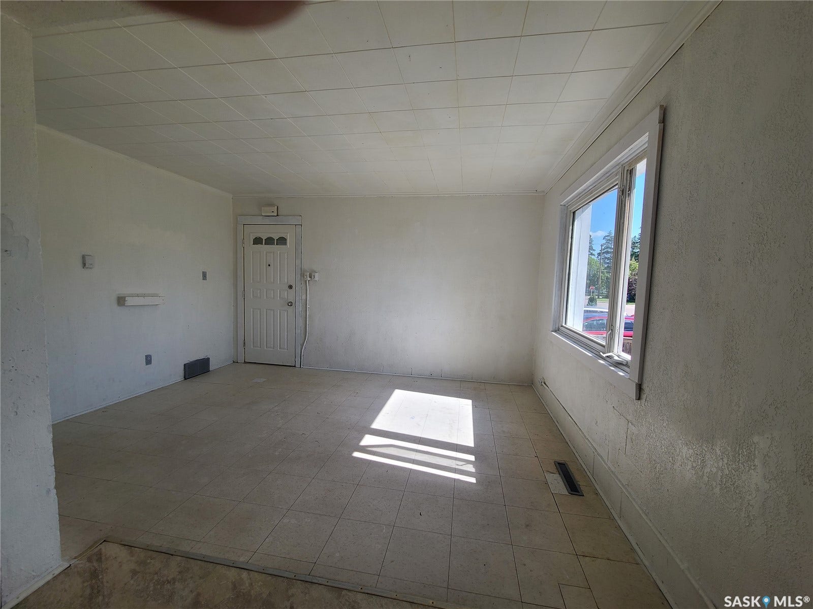 Tiled flooring throughout, white paneled entrance door with decorative lites, single-pane window, and textured walls