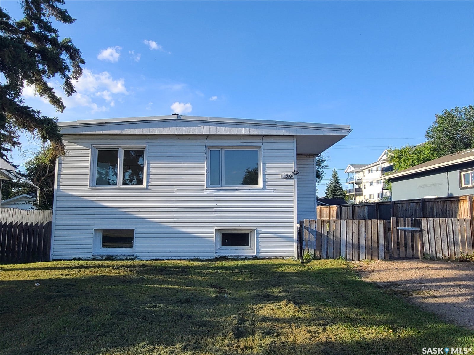 White siding exterior with multiple windows, a flat roofline, and a partially fenced yard