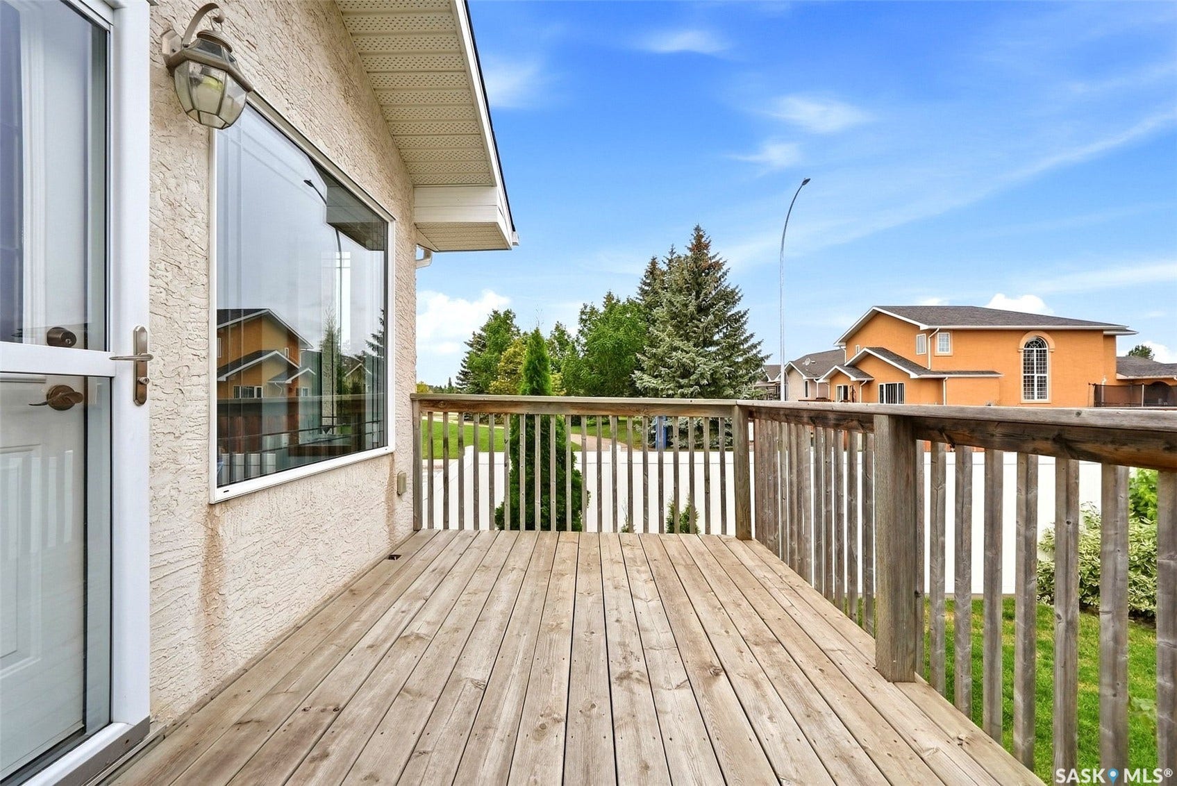 Expansive wood deck with a full railing, directly accessible via a white exterior door, featuring a large window