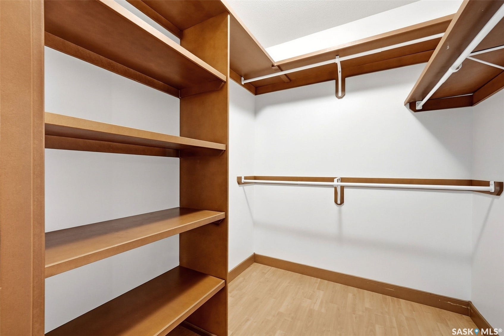 Built-in shelving, multiple hanging rods, and wood-finish flooring