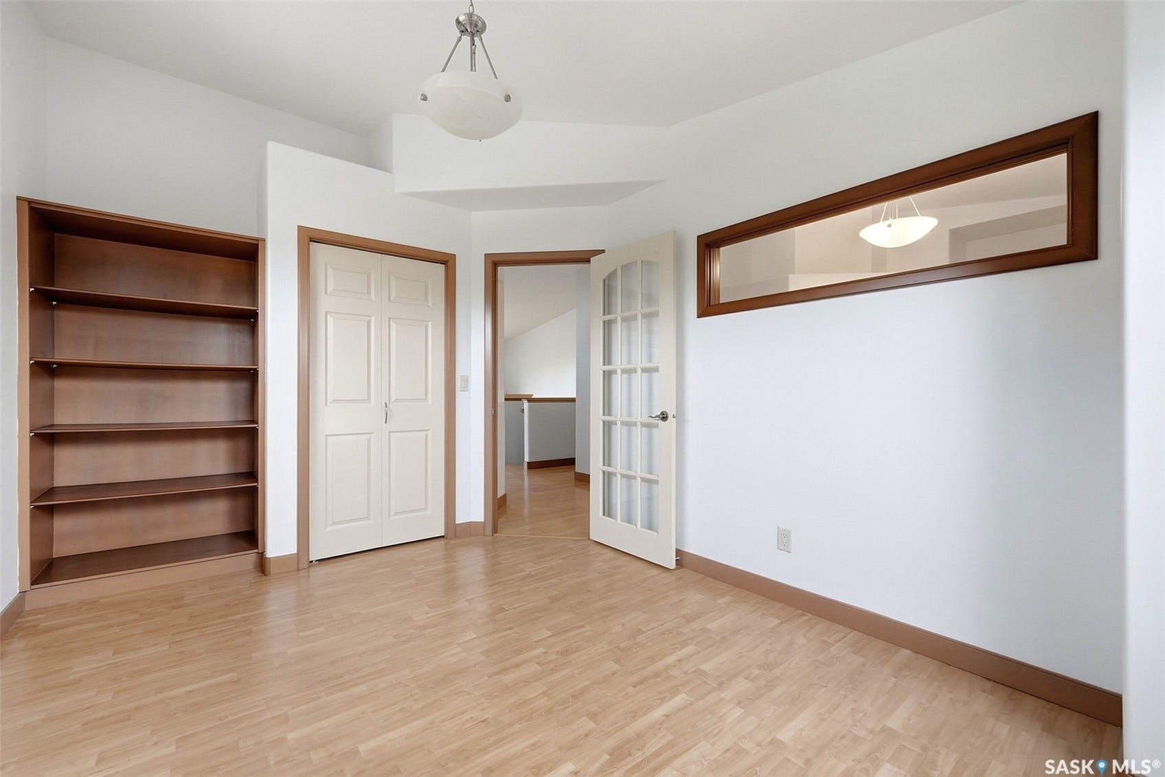 Built-in shelving, wood-finish flooring, two-panel bifold door, French door with glass panes, and a transom window with wood trim