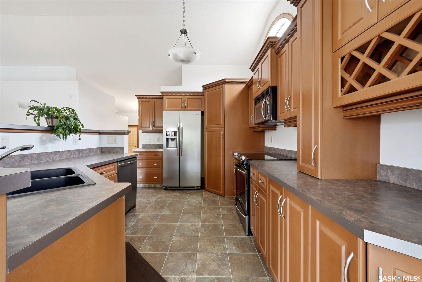 Kitchen featuring wood-finish cabinetry, stainless steel appliances, a double basin sink, and tile flooring