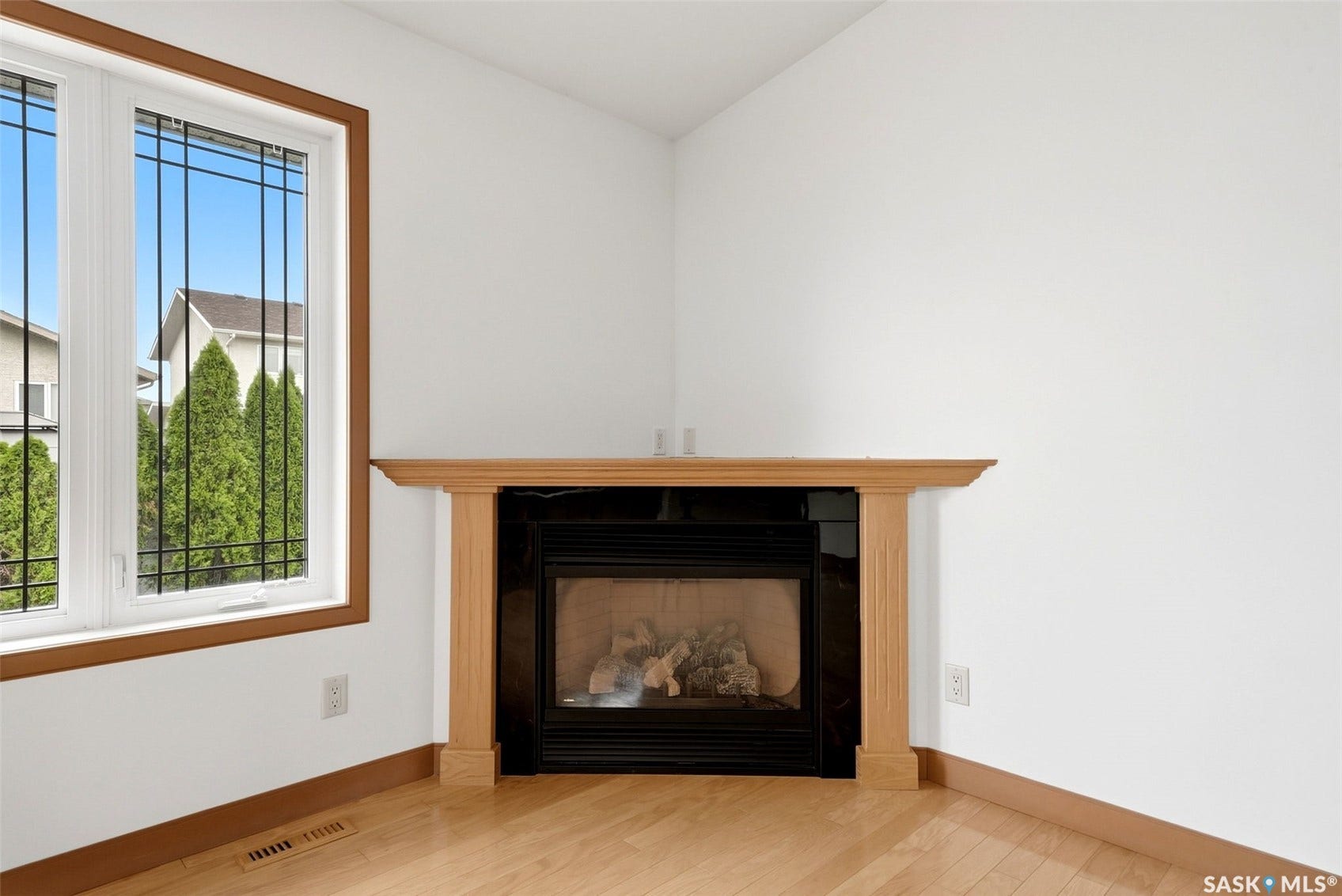 Corner fireplace with a light wood mantelpiece and dark tile surround, set against white walls, with wood-finish flooring