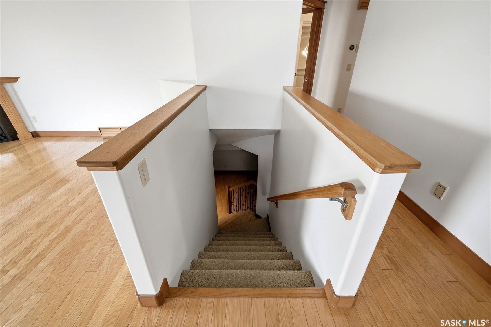 Wood-finish flooring, white walls, and a wood-finish stair railing