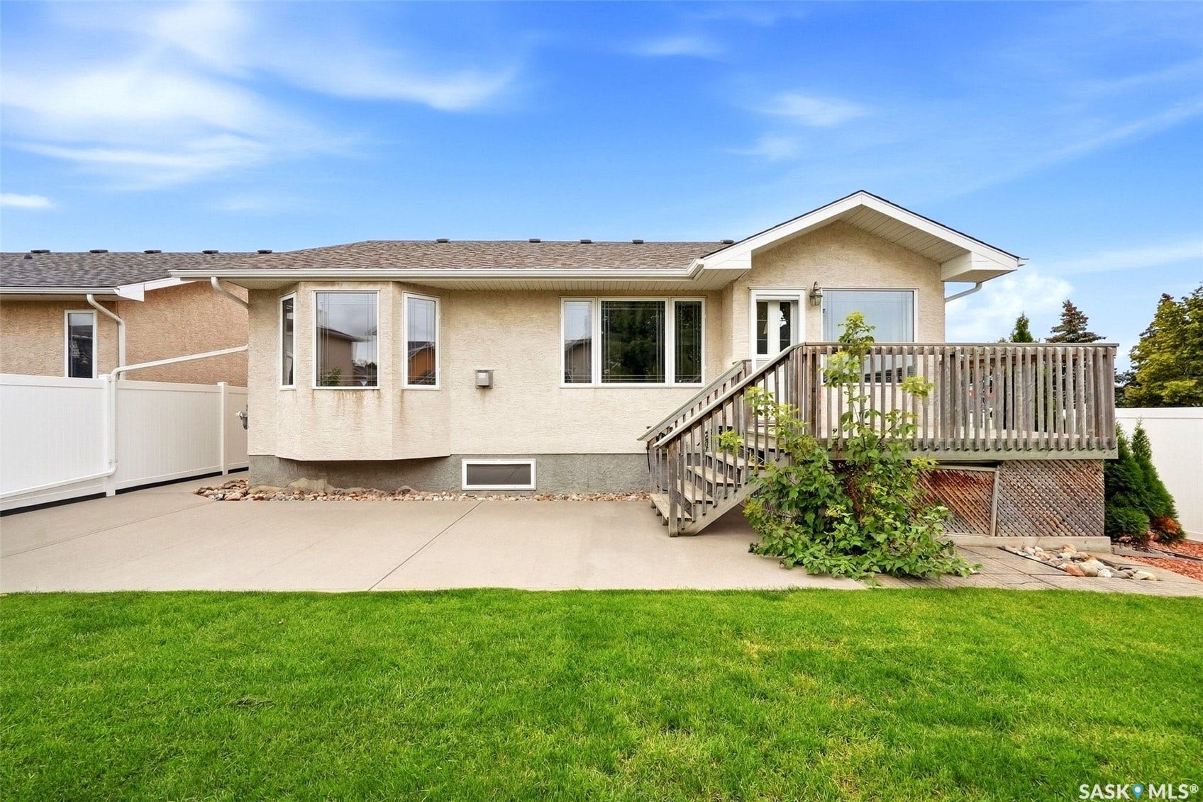 Expansive backyard featuring a manicured lawn, concrete patio, and a wooden deck with stairs