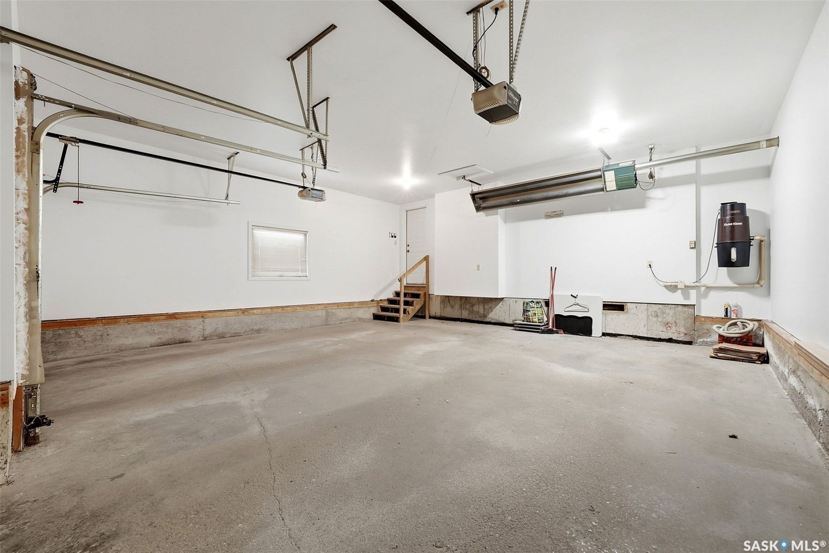 Spacious garage with concrete flooring, overhead garage door mechanisms, and built-in wall vacuum system
