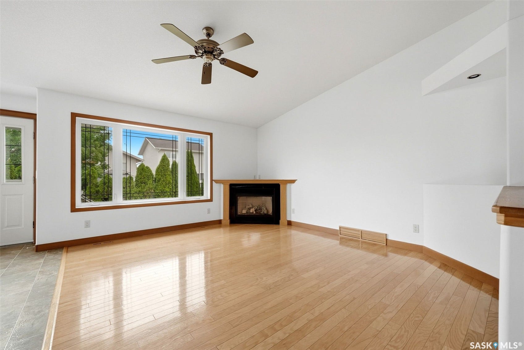 Hardwood flooring, natural wood trim, a built-in fireplace, a ceiling fan, and a transom window above the entry door