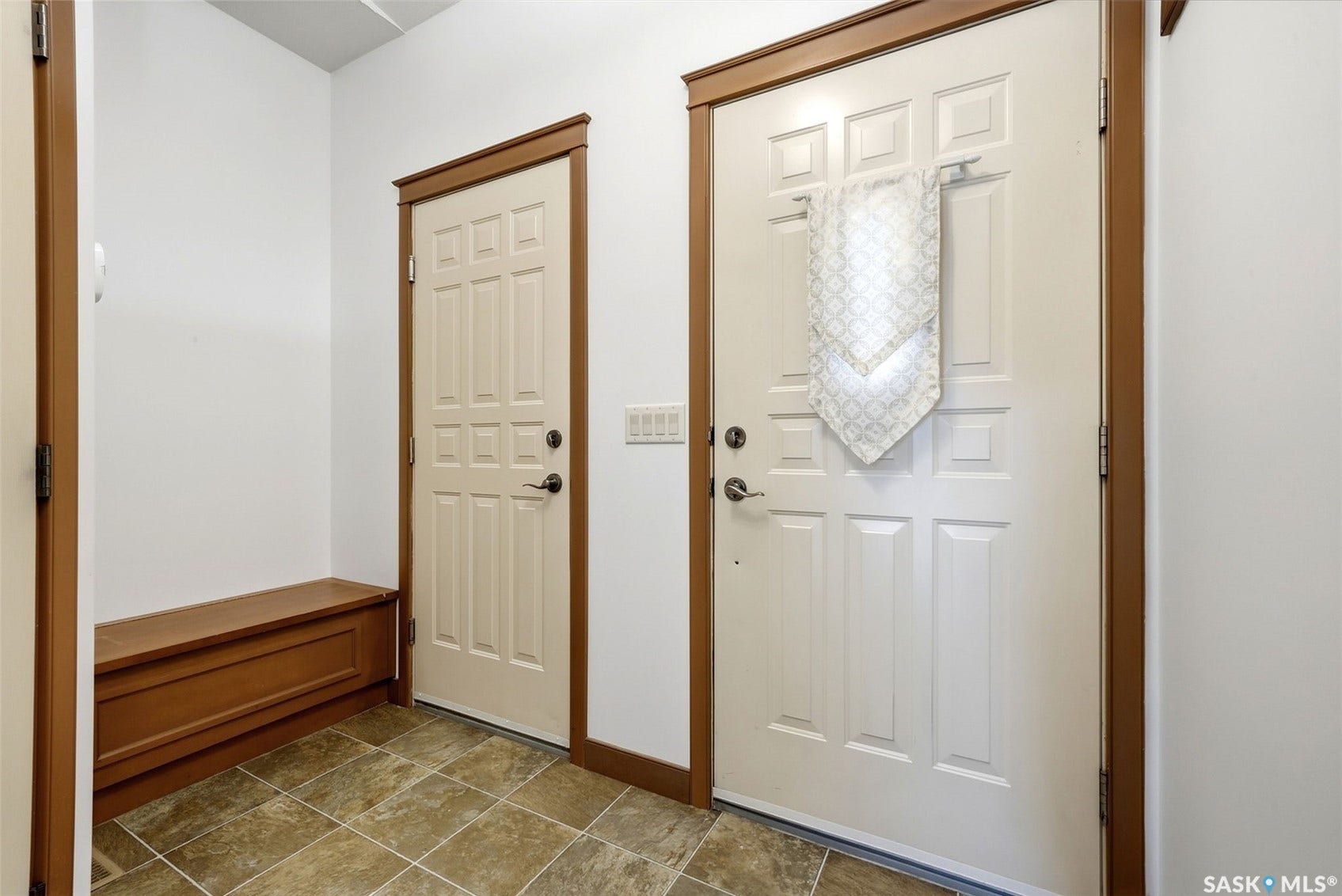 White panel doors with wood-finish trim, built-in wooden bench, and square-tiled flooring