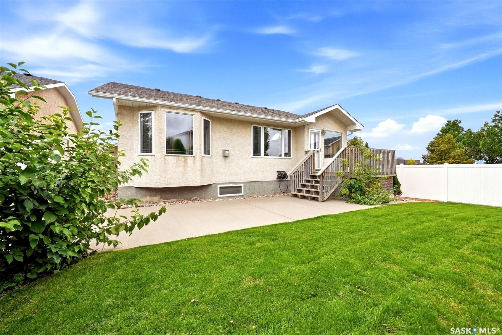 Expansive green lawn, stucco exterior, multi-level wood deck, white privacy fence, and large bay windows