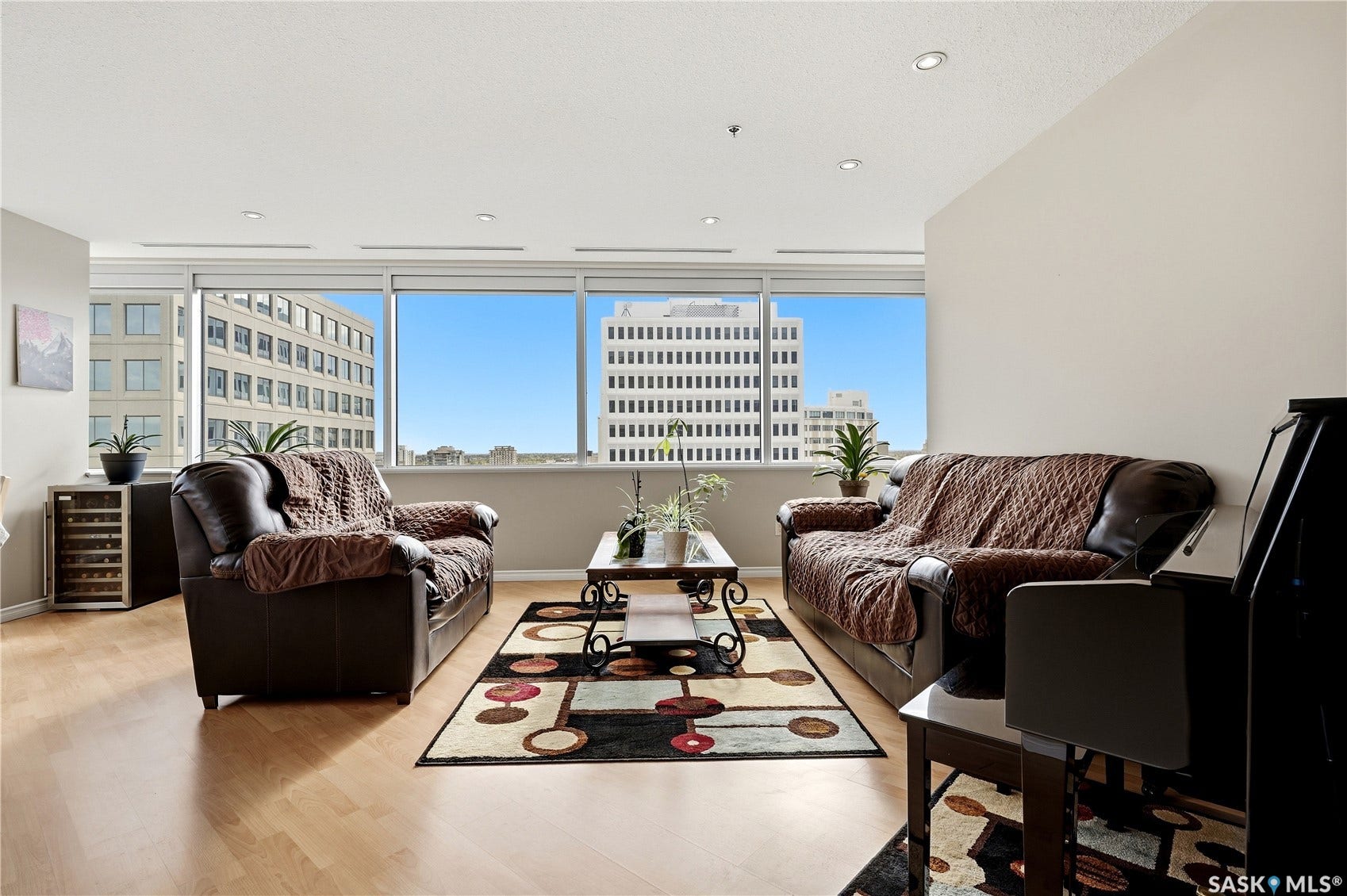 1914 Hamilton Street, #1007, Regina SK S4P 3N6 Expansive windows framing urban buildings, light wood-finish flooring, recessed ceiling lighting, and neutral wall tones
