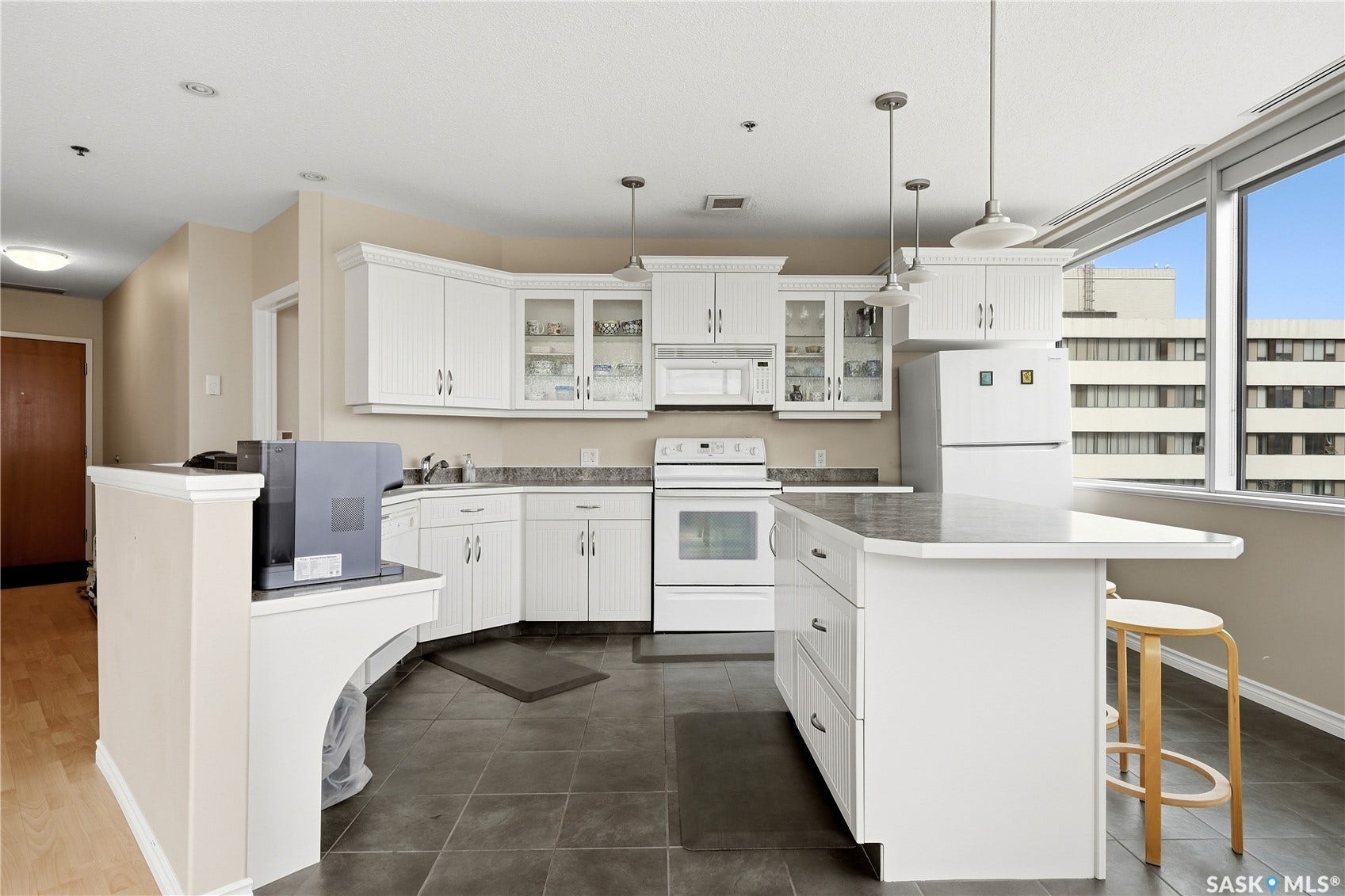 1914 Hamilton Street, #1007, Regina SK S4P 3N6 Kitchen featuring white cabinetry, dark tile flooring, white appliances, a center island with an extended countertop, and large windows