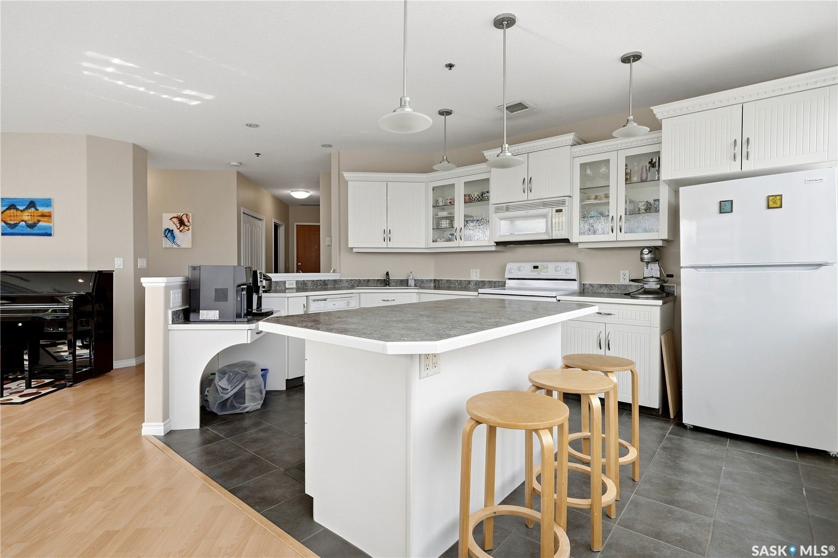 1914 Hamilton Street, #1007, Regina SK S4P 3N6 White cabinetry with glass-front accents, dark-toned countertop surfaces, pendant lighting fixtures, and a central kitchen island