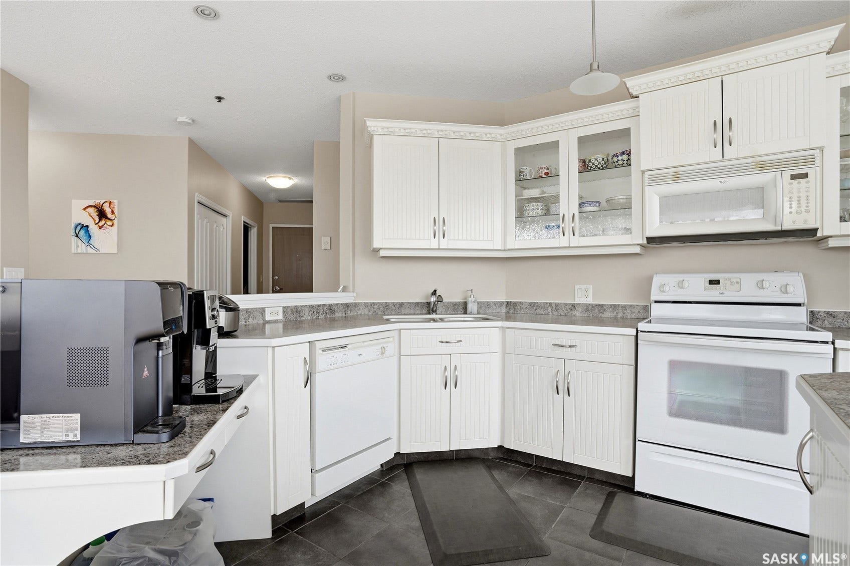 1914 Hamilton Street, #1007, Regina SK S4P 3N6 White beadboard cabinetry, gray speckled countertops, white built-in microwave, white electric range, and dark tile flooring