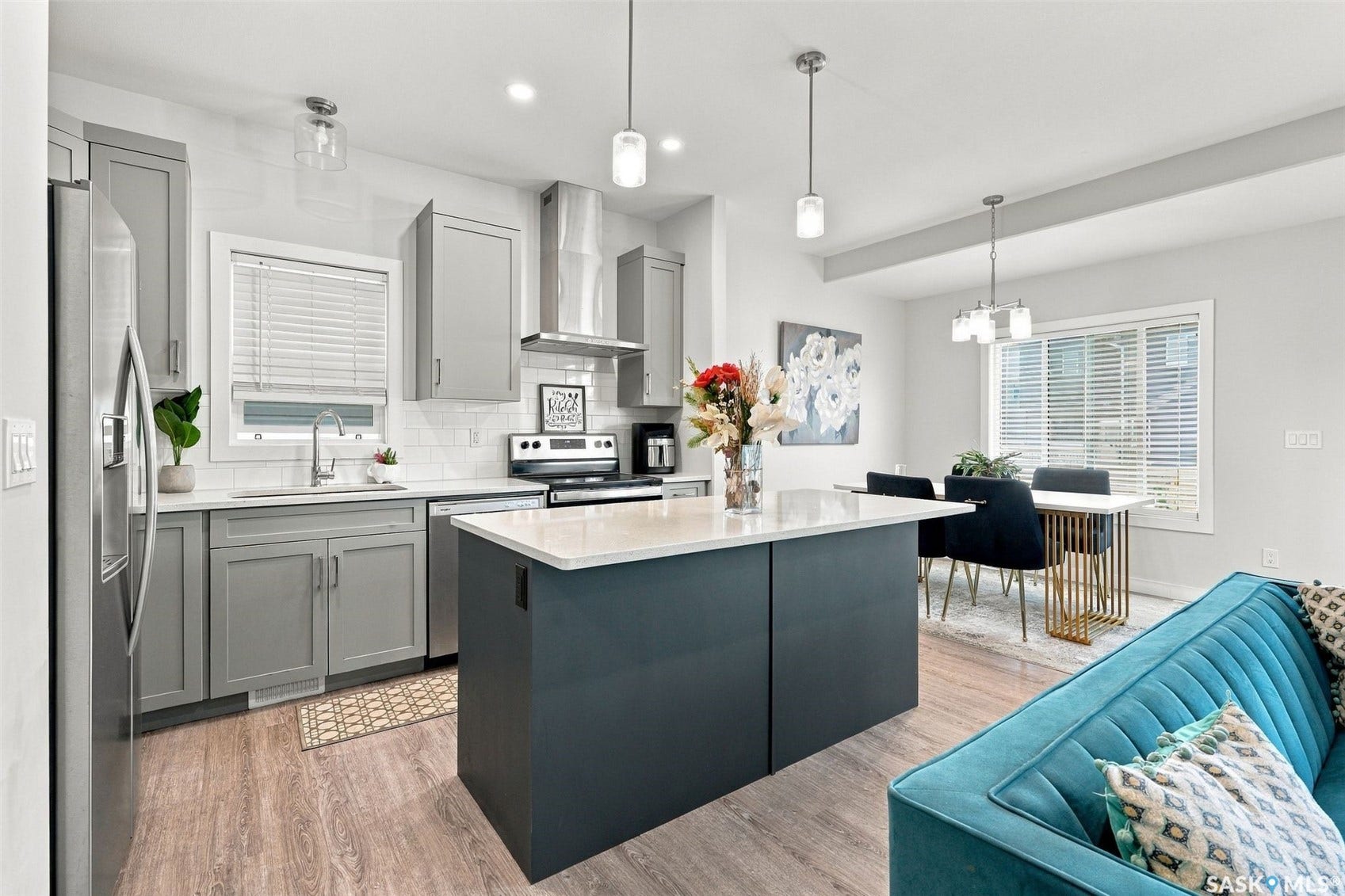Open-concept kitchen featuring an island with a light-toned countertop, gray cabinetry, stainless steel appliances, and wood-finish flooring
