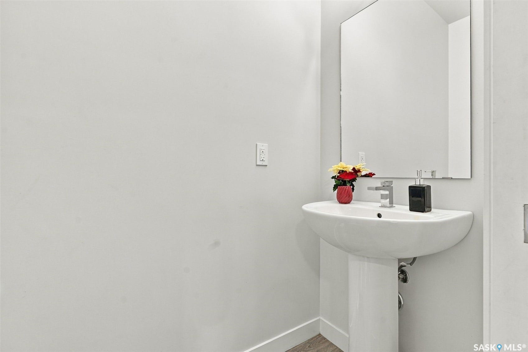 Pedestal sink with a polished chrome faucet and an unframed wall mirror