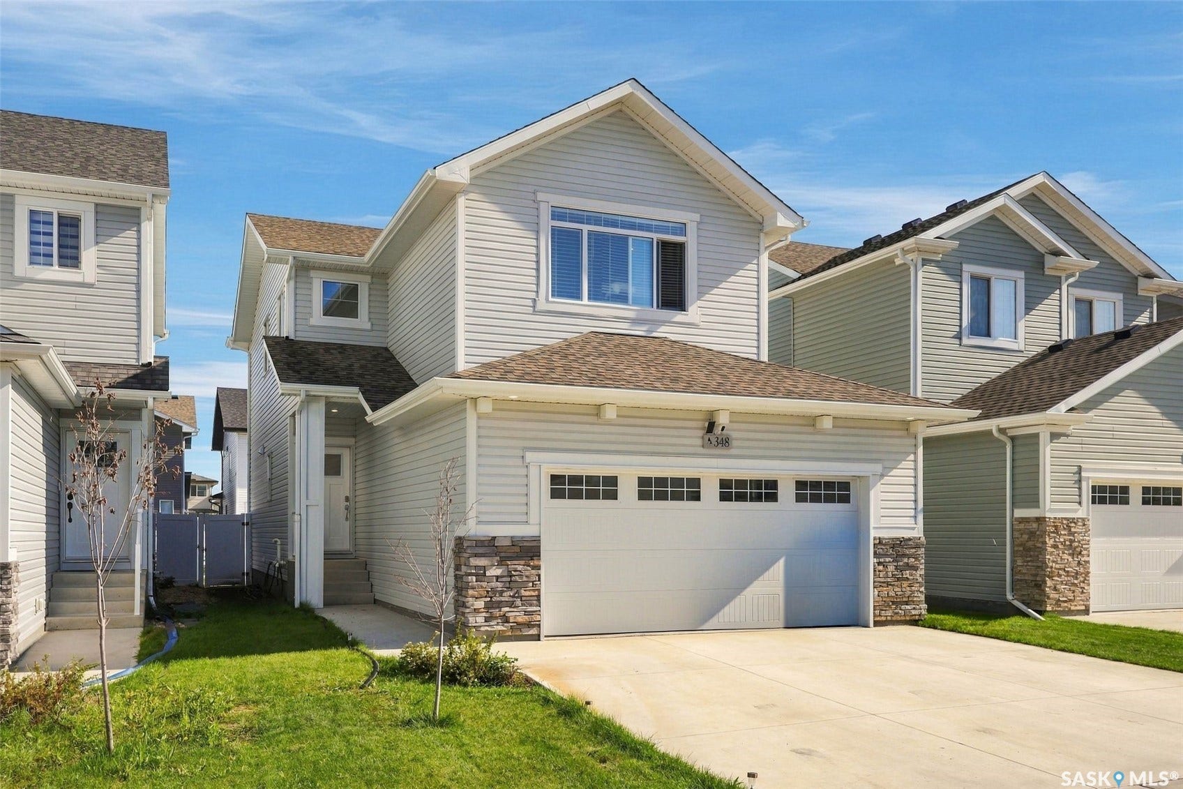Light-colored siding exterior with stone accent detailing, attached two-car garage, and a concrete driveway